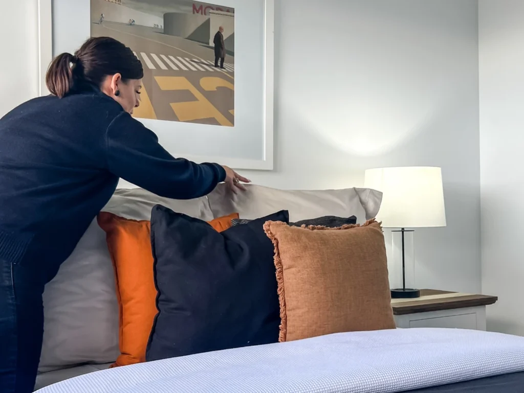 A woman putting pillows on a bed.