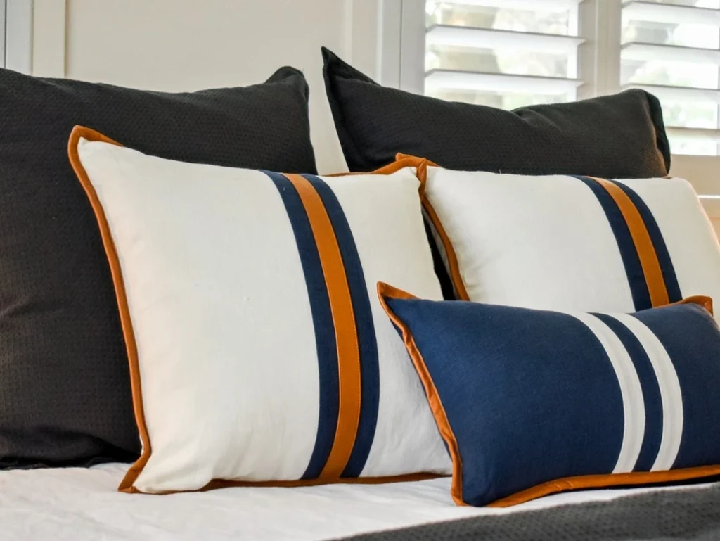 A bed with blue, white and orange striped pillows.